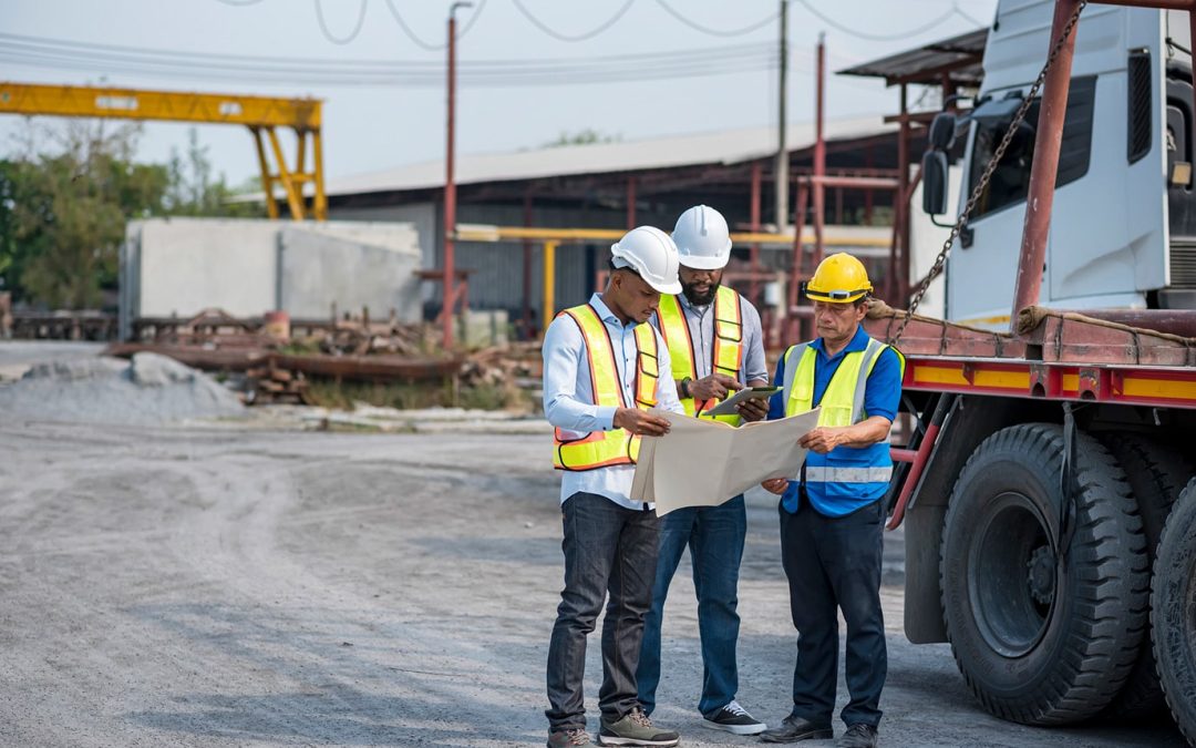 Three male contractors in safety vest huddled reviewing blueprint